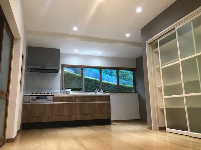 B様邸 キッチン・床・クロス・収納棚一新リフォーム施工後（宇陀市）— 木目のキッチンと窓の緑が抜ける開放的な空間